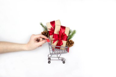 Hediyeler, köknar kozalakları, ladin dalları beyaz arka planda izole bir şekilde duran el arabası, kopyalama alanı. Süpermarket tramvayı ile yaratıcı noel kompozisyonu. Noel alışveriş konsepti