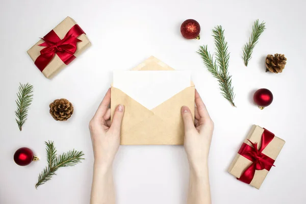 手は封筒と手紙を保持します 贈り物 モミのコーン トウヒの枝 赤い装飾フラットは白い背景に孤立し スペースをコピーします クリスマス招待状 新年おめでとう クリスマスのお祝いのコンセプト — ストック写真