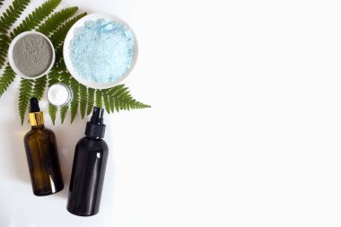 Deniz tuzu, kil, krema, kahverengi damlalık bardakta serum, yeşil eğrelti otu düz beyaz arka plan manzaralı, kopyalama alanı. Spa ürünleri. Organik, doğal kozmetik. Güzellik, cilt bakımı.