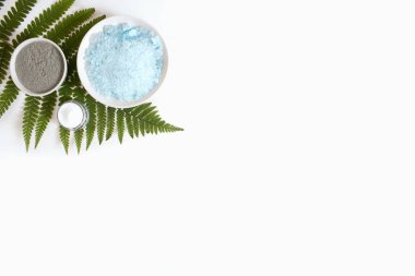 Deniz tuzu, kil, krema, kahverengi damlalık bardakta serum, yeşil eğrelti otu düz beyaz arka plan manzaralı, kopyalama alanı. Spa ürünleri. Organik, doğal kozmetik. Güzellik, cilt bakımı.