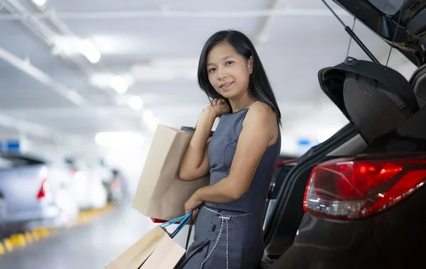 アジアの女性は 車の後ろの買い物袋をしてください 駐車場はショッピング モールです — ストック写真