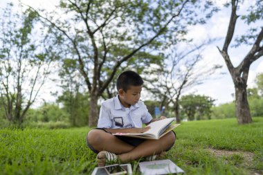 Asyalı çocuk parkta kitap okuyor..