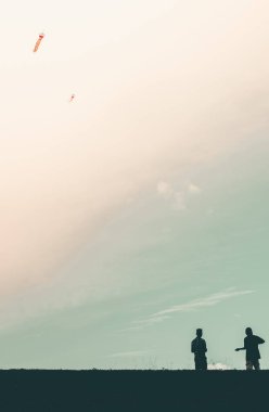 Akşamları nehir kıyısında uçurtma uçuran iki çocuğun silueti.
