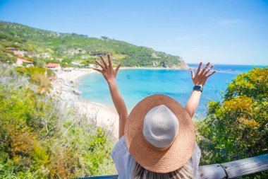 Akdeniz kıyısı arka planında hasır plaj şapkalı bir kadın. Yaz tabelası. Meditasyon ve rahatlama. Tatil ve turizm konsepti. 