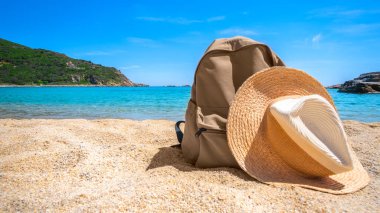 Plaj hasır şapkası ve sırt çantası okyanus sahili arka planında. Mesaj için yer var. Tatil ve turizm konsepti. Güneş çarpması koruyucu aksesuar