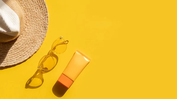 Güneş koruma nesneleri. Güneş gözlüklü saman kadın şapkası ve parlak sarı arka planda spf kremi üst görünümü. Plaj aksesuarı. Yaz Seyahati Konsepti. İndirim seti. Boşluğu kopyala. 