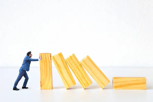 Miniature businessman figure is holding falling wooden planks on white background. Solving the problem of economic business crisis, progress, survival