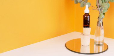 Ahşap kaide ve okaliptüs dalları üzerinde turuncu arka planda cam vazoda serum koyu şişe. Kozmetik ürünleri. Deri iyileşmesi için organik doğal tedavi