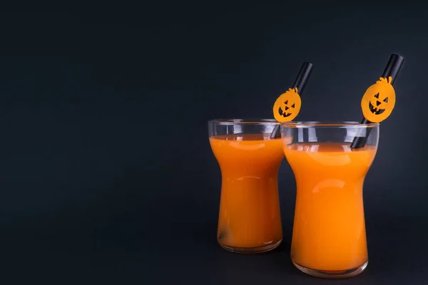 Halloween carbonated orange beverage in glass decorated with black tube and jack-o-lantern pumpkin on dark background. Homemade party Punch cocktail. Space for text