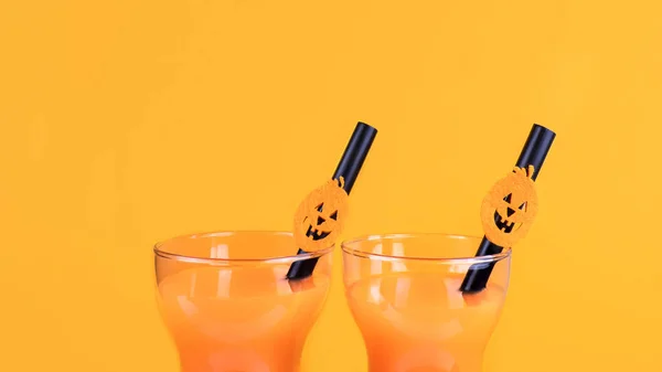 Halloween carbonated orange beverage in glass decorated with black tube and jack-o-lantern pumpkin on orange background. Homemade party Punch cocktail. Copy space