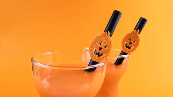 Halloween carbonated orange beverage in glass decorated with black tube and jack-o-lantern pumpkin on orange background. Homemade party Punch cocktail. Copy space. Close up