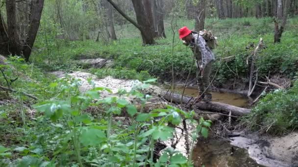 Mature man traveler with backpack cautiously crosses through stream of wood logs — Stock Video