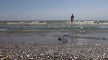 Neşeli kız bikini bir süpermarket arabası geçmiş yaz denizin dalgaları üzerinde çalışır
