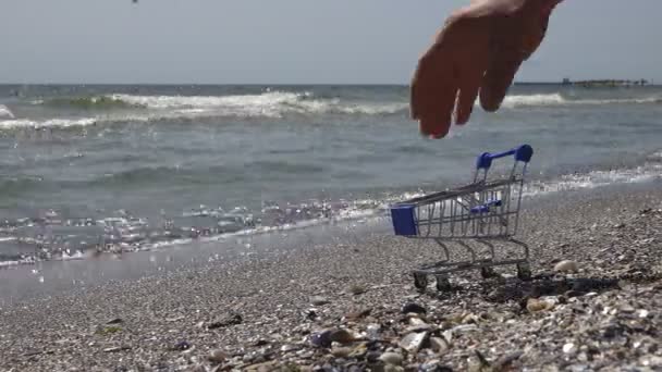 Mans Hand Picks Up Supermarket Trolley From A Grocery Store That Stood On Sea Or Ocean With A Cargo Ship On Horizon And Fishing Nets