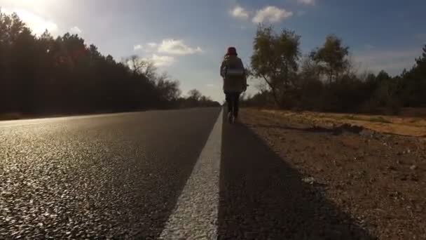 年轻女孩 游客搭便车的人背着一个背包沿着公路走着 举起大拇指 旅行者试图停车 在夏天森林的高速公路 — 图库视频影像