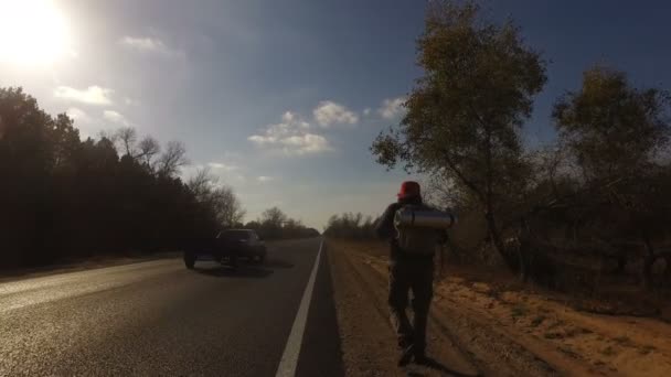 中年の男性 観光ヒッチ ハイカーに沿って歩くバックパック道路彼の肩の上を持ち上げるタブレット 旅行者が車を停止しようとしています 夏の森の高速道路 — ストック動画