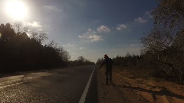 中年の男性 観光ヒッチ ハイカーに沿って歩くバックパック道路彼の肩の上を持ち上げるタブレット 旅行者が車を停止しようとしています 夏の森の高速道路 — ストック動画