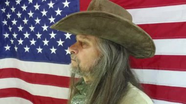 Vatansever portresi - olgun bir adam, uzun saçlı, sakallı ve şapkalı bir kovboy Amerikan bayrağının arka planında