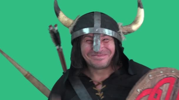 Šílený Viking v helmě s rohy, se štítem a velkou sekerou s veselým vzhledem tance a úsměvy. Portrét muže - zelené pozadí