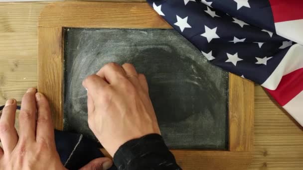 Eine Männerhand Schreibt Mit Kreide Auf Kreideteller Holzrahmen Neben Flagge — Stockvideo