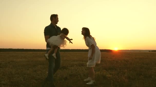 Eltern mit einem kleinen Kind spielen bei Sonnenuntergang außerhalb der Stadt. Mama, Papa und Kind lachen zusammen. Wochenenden mit der Familie. Teamarbeit — Stockvideo