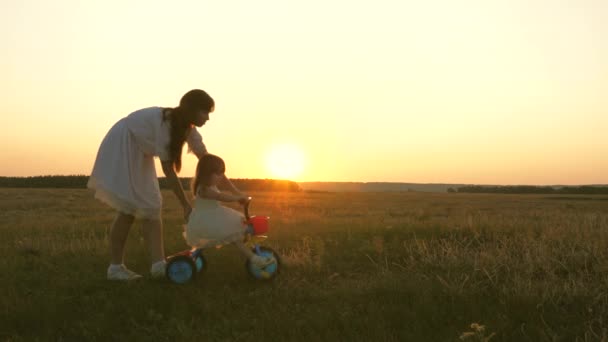 엄마는 공원에서 해질 녘에 자전거타는 법을 어린 아이에게 가르친다. 팀워크. 실루엣 가족의 산책 — 비디오