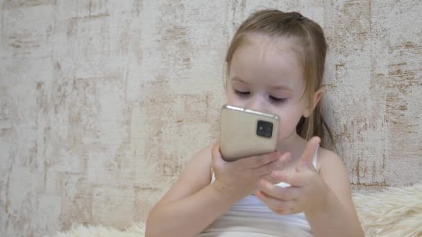 The girl communicates with the parent via a smartphone online. The child kisses the phone, waves and talks through the video connection of the phone. Remote conversation — Stock Video