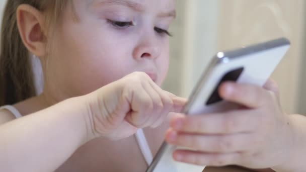 En liten flicka spelar i en smartphone. Barnet lär sig på distans i telefonapplikationen. Förskollärare på Internet — Stockvideo