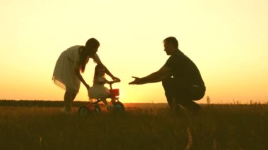 Gün batımında ailesiyle birlikte bisiklete binen bir çocuğun silueti. Anne, baba ve bebek akşam parkında oynuyorlar. Mutlu aile hayatı. Takım çalışması.