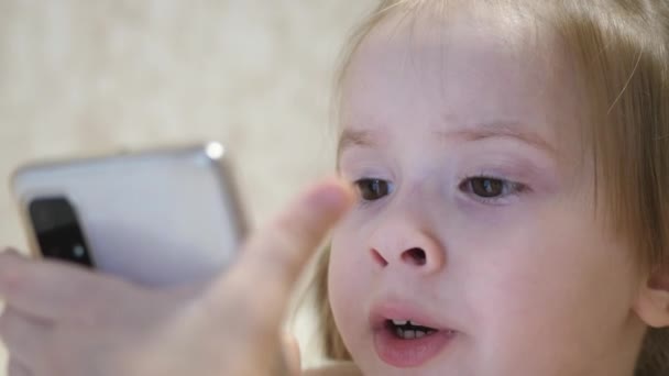 Uma criança pequena está falando ao telefone via videochamada. Kid se comunica remotamente através de um aplicativo móvel. Educação pré-escolar usando a Internet. Close-up — Vídeo de Stock