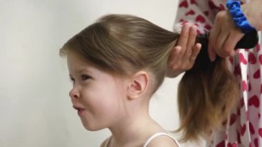 Annem bebek saçlarını tarar ve lastiğin üzerinde at kuyruğu şeklinde toplar. Aile sabahı. İşleri yoluna koymak. Ebeveyn, kızı saç stili yapar. Yakın plan.