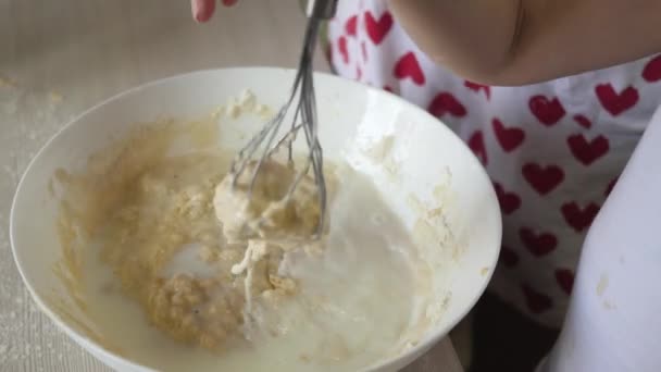 Mamma lär ett barn att laga stålar. Mor och barn slår med en visp en massa mjöl med mjölk. Matlagning hemma med familjen. Lagarbete — Stockvideo
