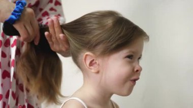 Annem bebek saçlarını tarar ve lastiğin üzerinde at kuyruğu şeklinde toplar. Aile sabahı. İşleri yoluna koymak. Ebeveyn, kızı saç stili yapar. Yakın plan.