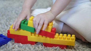 Yerde oturan inşaatçıda bir çocuk oynuyor. Oyuncak bebek. Anaokulu eğitimini geliştirme ve düşünme. Küçük bir çocuk çok renkli tuğlalardan inşa eder. Yakın plan.