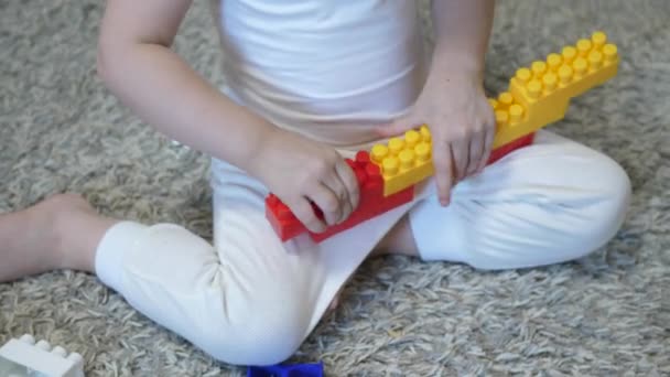 Een kind speelt in de bouwer zittend op de vloer. Speelgoedbaby. Ontwikkeling en denken aan kleuteronderwijs. Een klein kind bouwt van veelkleurige stenen. Close-up — Stockvideo