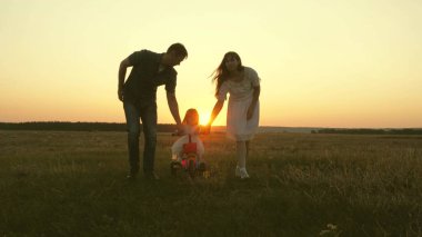 Anne ve baba küçük bir çocuğa gün batımında parkta bisiklet sürmeyi öğretiyor. Takım çalışması. Siluet aile yürüyüşü