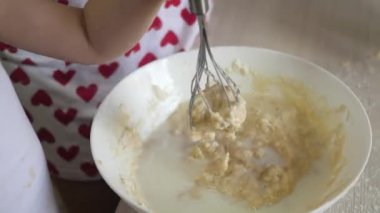Anne bir çocuğa hamur pişirmeyi öğretiyor. Anne ve çocuk çırpılmış bir çırpıda bir parça un ve sütle dövülmüş. Evde ailenle yemek pişirmek. Takım çalışması.