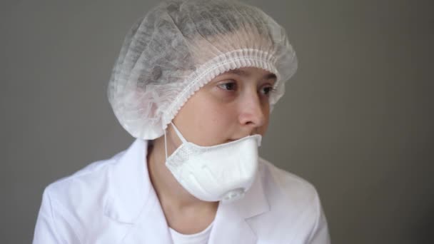 Odpočívá mladý doktor v županu s čepicí a obličejovou maskou. Zdraví, medicína a pandemie. Kovid-19. Detailní záběr — Stock video