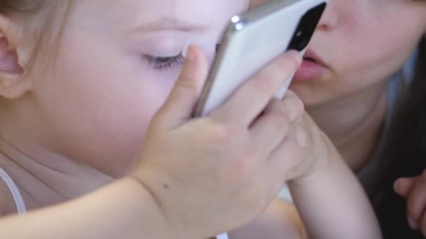 Ett litet barn kommunicerar på distans via telefon och kysser sin mamma. Spel i moderna prylar för barn. Utveckling och skapande av ett barn i en smartphone. Närbild — Stockvideo