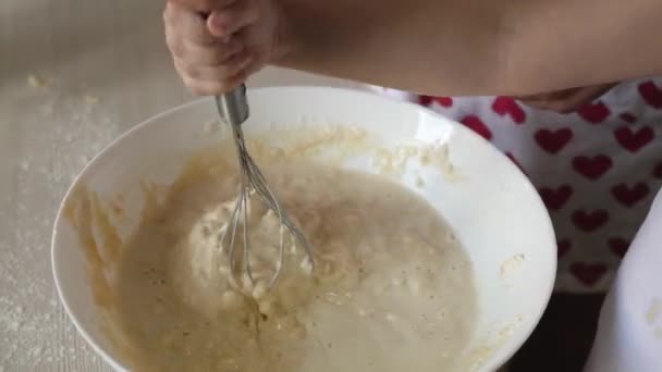 Mamá enseña a un niño a cocinar masa. Madre e hijo golpean con un batidor una masa de harina con leche. Cocinar en casa con la familia. Trabajo en equipo — Vídeo de stock