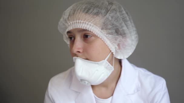 Un jeune médecin en peignoir avec une casquette et un masque est assis au repos. Santé, médecine et concept de pandémie. Kovid-19. Gros plan — Video