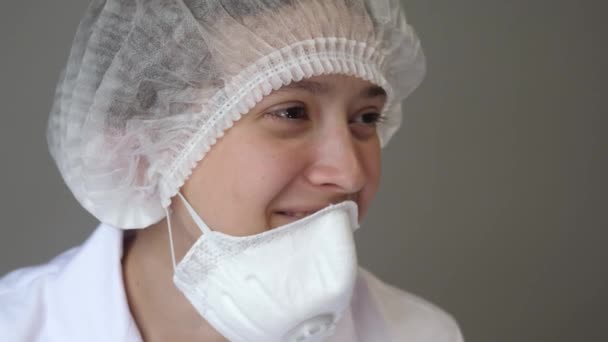 Un jeune médecin en manteau avec une casquette et un masque est assis au repos et souriant. Santé, médecine et concept de pandémie. Kovid-19. Gros plan — Video