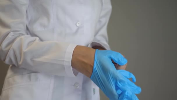 Ein Arzt im Morgenmantel zieht sich blaue sterile Handschuhe aus Naturlatex über. Gesundheit, Medizin und Pandemiekonzept. Covid-19. Nahaufnahme — Stockvideo