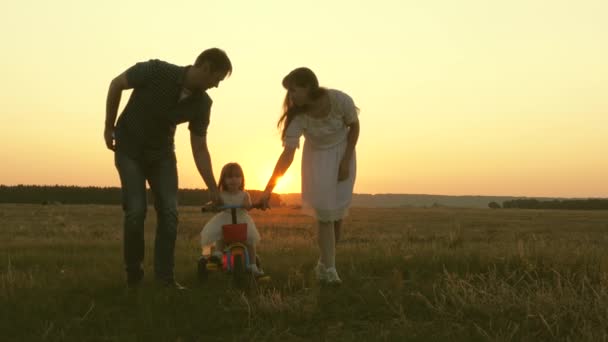 Mama und Papa bringen einem kleinen Kind bei, bei Sonnenuntergang im Park Fahrrad zu fahren. Teamwork. Familienspaziergang mit Silhouette — Stockvideo