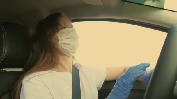 为防止COVID-19的传播，年轻妇女戴着医疗面罩开车。驾驶带着面具和手套的女司机，以防止感染流感病毒 — 图库视频影像