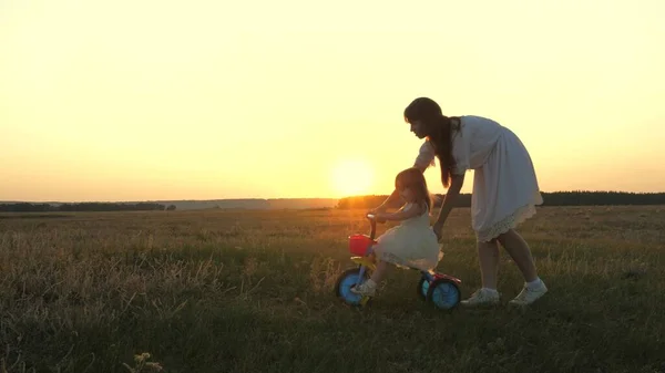 Мама учит маленького ребенка кататься на велосипеде на закате в парке. Командная работа. Силуэт семейная прогулка — стоковое фото