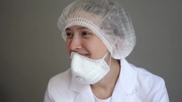 Un jeune médecin en manteau avec une casquette et un masque est assis au repos et souriant. Santé, médecine et concept de pandémie. Kovid-19. Gros plan — Video