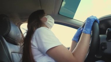 Tıbbi maskeli ve mavi eldivenli bir kadın araba kullanıyor. Kız dans ediyor ve şarkı söylüyor. Covid-19. Salgın