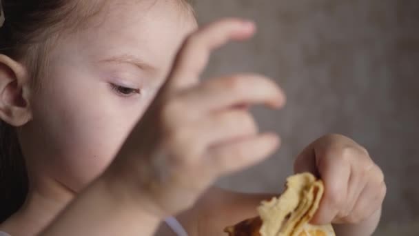 En liten flicka äter hembakade pannkakor och slickar sitt finger. Hemlagad mat i köket. Mjöl för barn. Närbild — Stockvideo