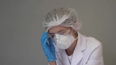 Maske, mavi eldiven, beyaz önlük, gözlük ve şapka takan bir sağlık görevlisi. Yorgun hemşire. Covid-19. Salgın